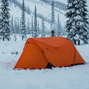 A sturdy backpacking hot tent pitched in a snowy backcountry setting, providing shelter from winter conditions.