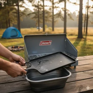 Removable porcelain-coated grate and griddle being taken off the Coleman stove for easy cleaning after use.