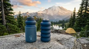 A high-detail 4K photorealistic close-up on a granite rock, showing two expanded blue collapsible silicone camping bottles; one has an insulating sleeve and a "COLD" graphic, the other is emitting steam from its mouth, illustrating their ability to hold hot and cold liquids.