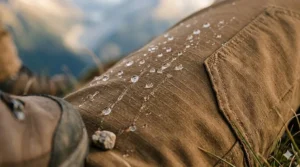 Close-up of the ripstop nylon fabric on a pair of men's hiking pants showing water droplets bead on the surface.