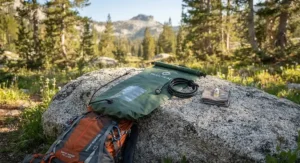 A lightweight, compact solar shower bag laid out on a rock next to a backpack, ready for a hiking trip.