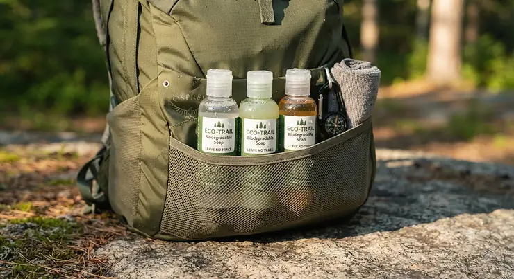 Travel-sized bottles of biodegradable soap for camping packed inside a backpack side pocket.