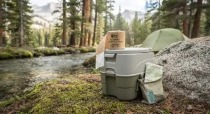 A portable camping toilet set up at a campsite with a roll of camping toilet paper ready for use.