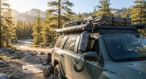 A pressurized portable camp shower mounted next to an SUV roof rack for overlanding and car camping.