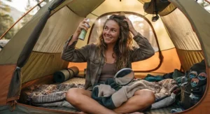 A young woman applying waterless dry shampoo inside her camping tent during a weekend getaway.
