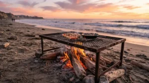 Friends gathered around a beach bonfire utilizing a low campfire cooking grate to roast vegetables.